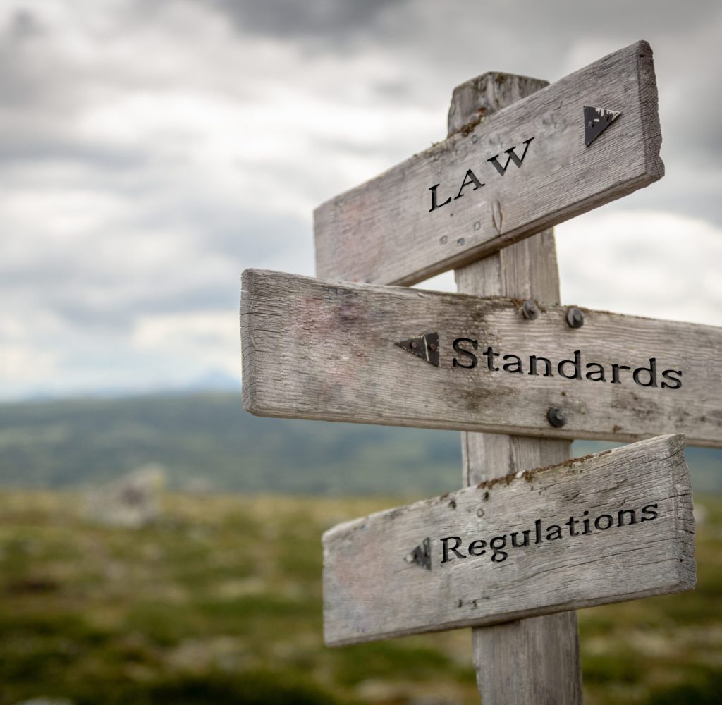 Law, standards and regulations text on wooden road sign outdoors in nature.