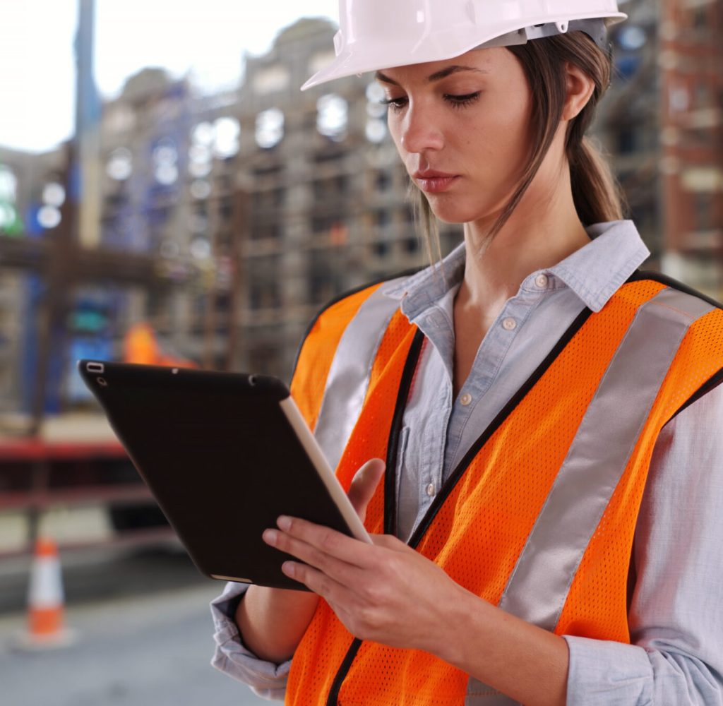 Focused female construction worker at work on pad device at construction site